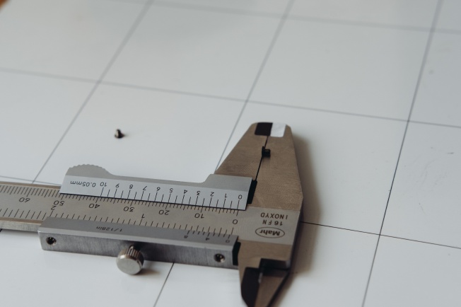 Measuring the thickness of the hat of the screw. Calipers indicate around 0.35mm.