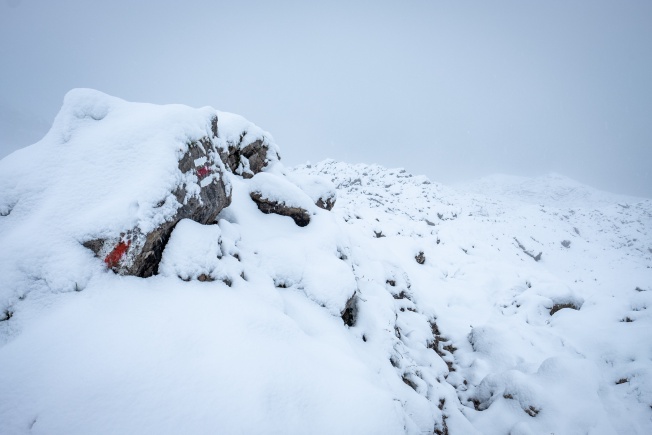 Trail markers painted onto the side of a rock. They are partially obscured by snow.