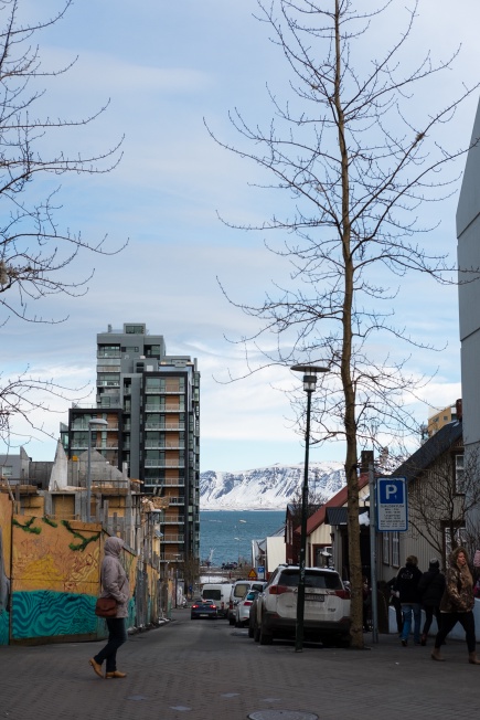 a street that looks like a shopping mall, with the ocean and a mountain in the background