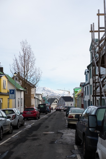 a backstreet with parked cars and a snow-capped mountain in the background